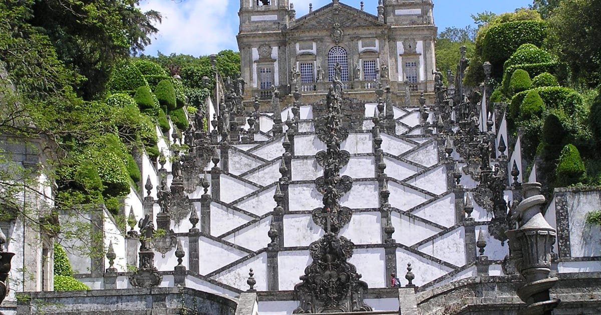 Escadório barroco em ziguezague do Santuário do Bom Jesus do Monte, em Braga, com as escadarias brancas, fontes e a basílica no topo da colina.