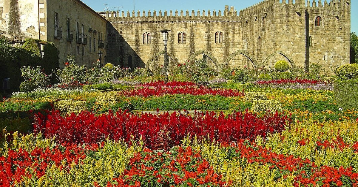 Jardim de Santa Bárbara em Braga, com canteiros floridos geométricos junto à ala medieval do Paço Episcopal e a fonte barroca encimada pela estátua de Santa Bárbara.