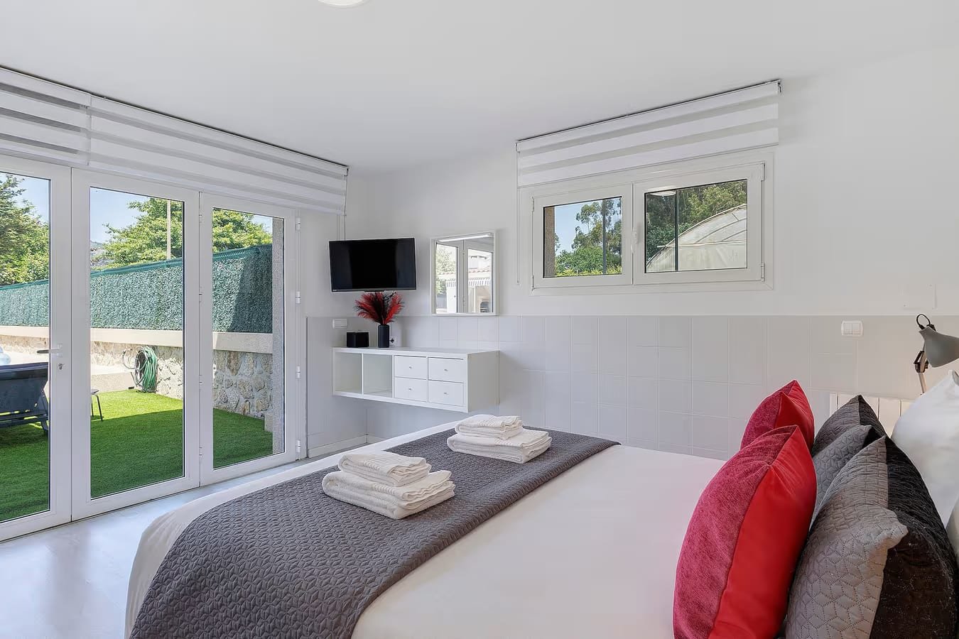 Quarto de casal do Alojamento Rio Neiva em Tregosa, Barcelos, com decoração em tons vermelhos e portas de vidro com vista para o jardim e a piscina.